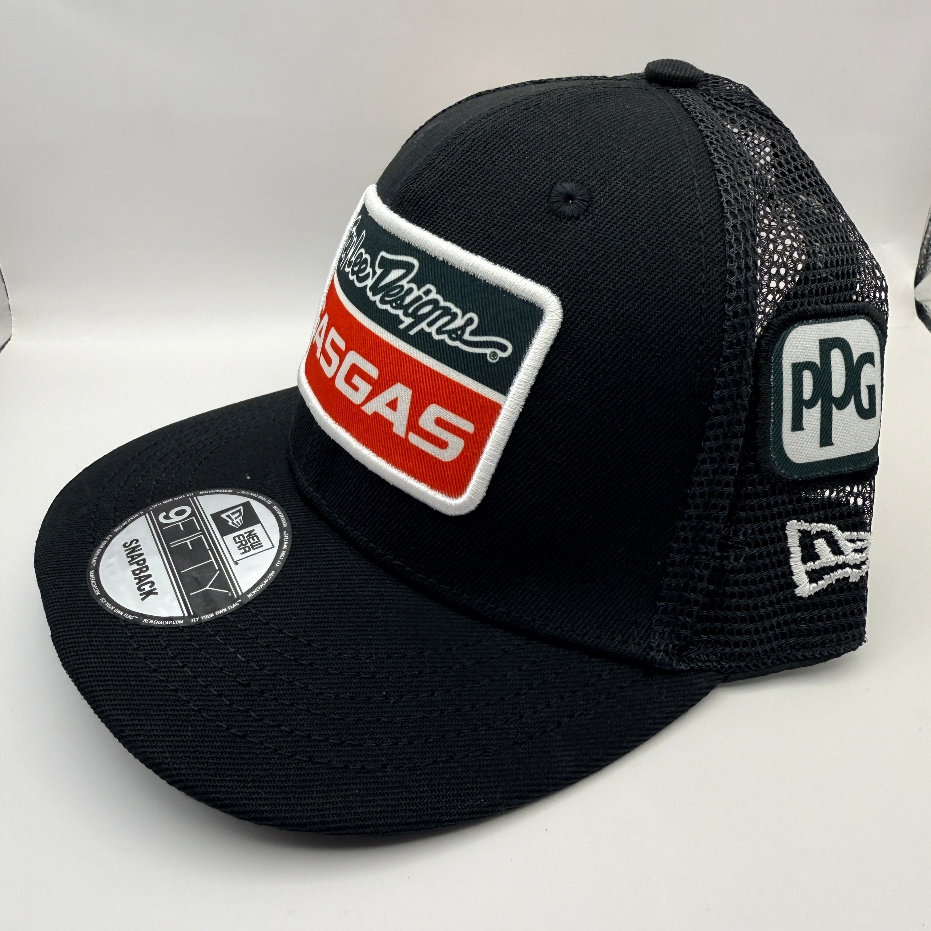 A black trucker-style baseball cap with a curved brim, featuring a large rectangular patch on the front with 'Tupelo' and 'MORGAS' in white, red, and black, a New Era 9FIFTY sticker on the brim, and a PPG logo patch on the side mesh back.